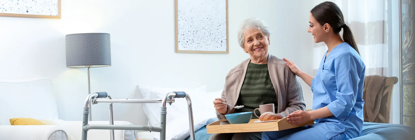 Carer serving breakfast to an older woman in her bedroom